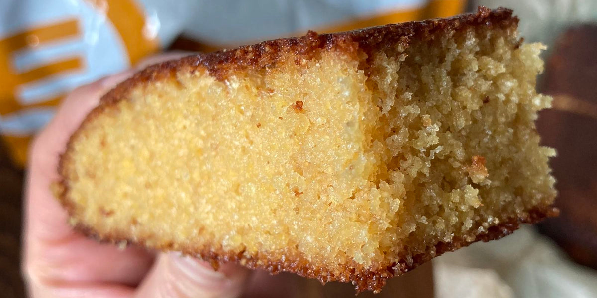 Slice of golden polenta cake held up in front of an orange bag
