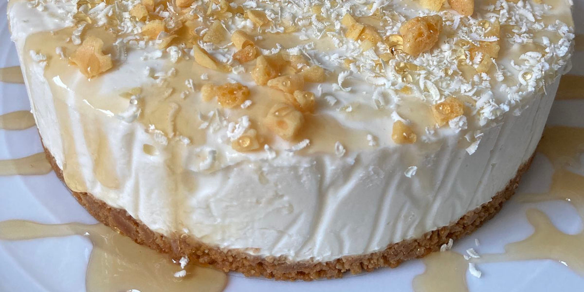 Round cheesecake on a biscuit base with white chocolate shavings and golden drizzle