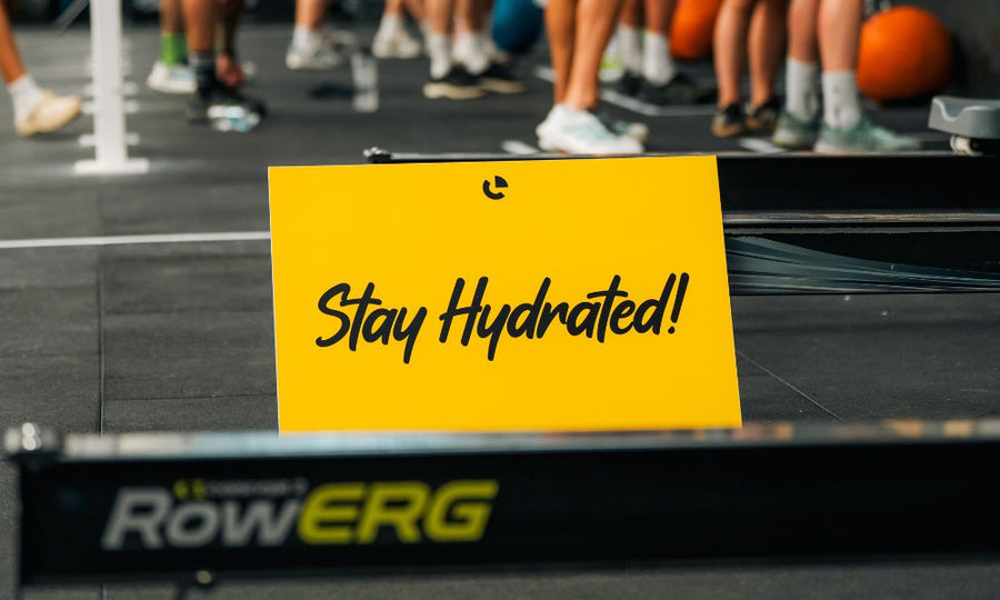 Yellow sign reading Stay Hydrated on a gym floor beside a rowing machine