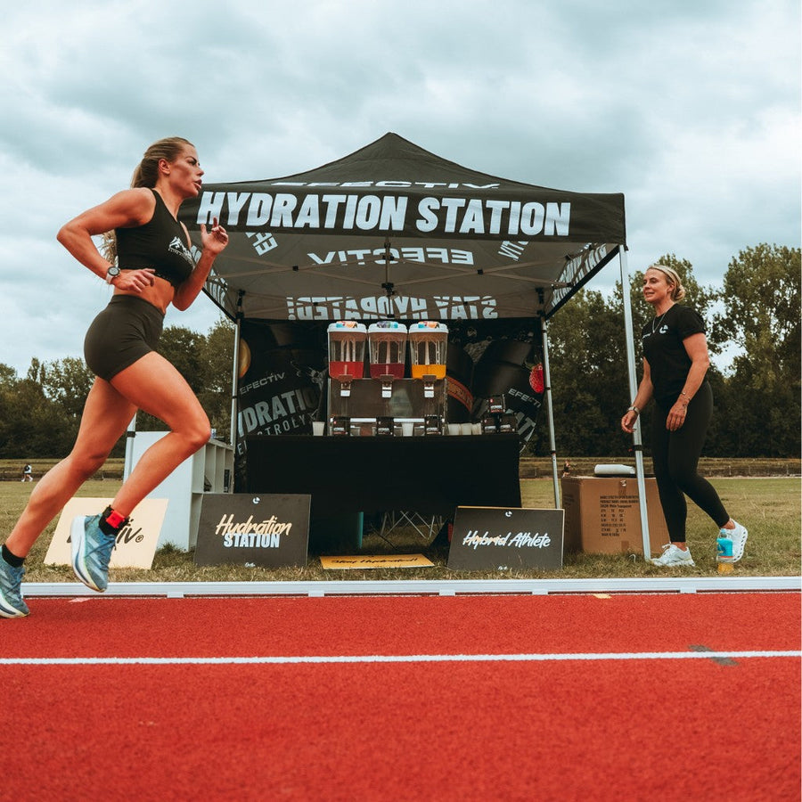 Woman running on a red track past an Efectiv Hydration Station tent